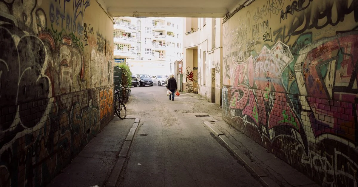 Ruelle berlinoise recouverte de graffitis, avec un piéton solitaire. Art urbain vibrant et ambiance trépidante.
