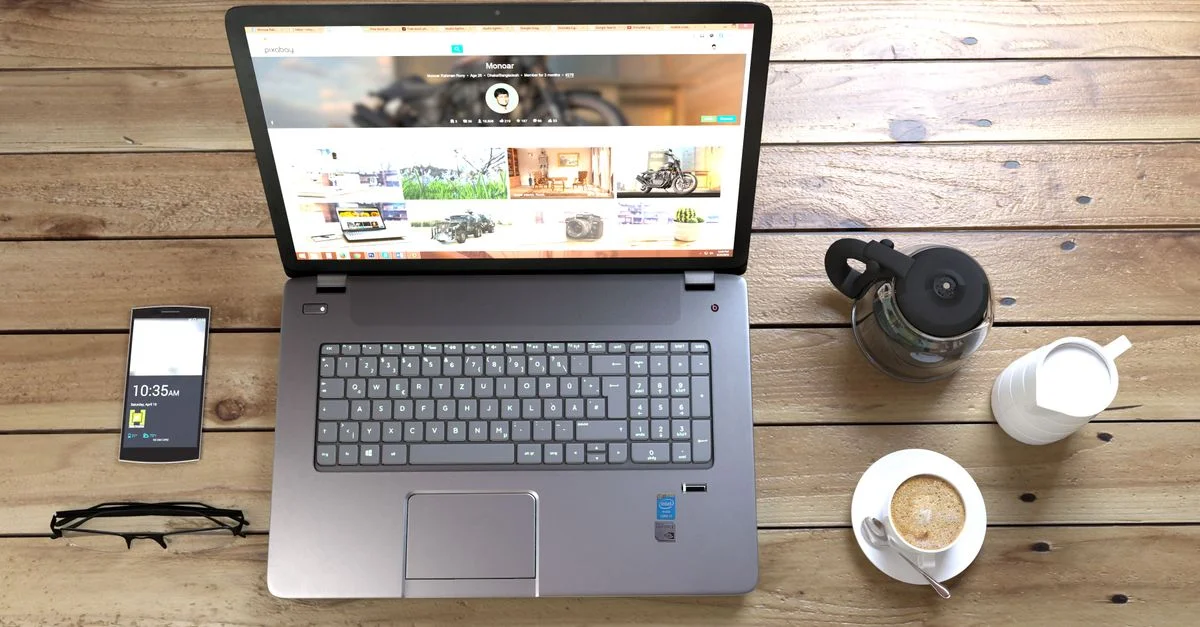 Vue de dessus d'un ordinateur portable, smartphone, café et lunettes sur un bureau en bois.