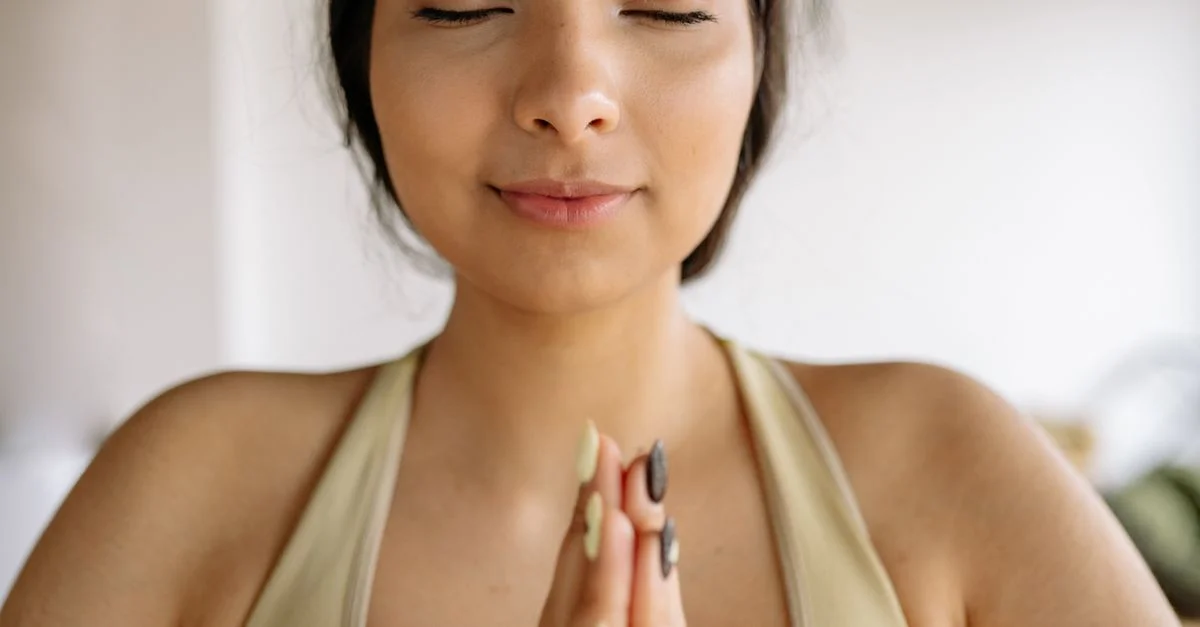 Une femme paisible méditant les yeux fermés dans une pose de yoga, adoptant la pleine conscience à l'intérieur.
