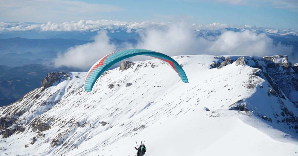 Un parapentiste survole une magnifique chaîne de montagnes enneigées, capturant l'essence même de l'aventure.